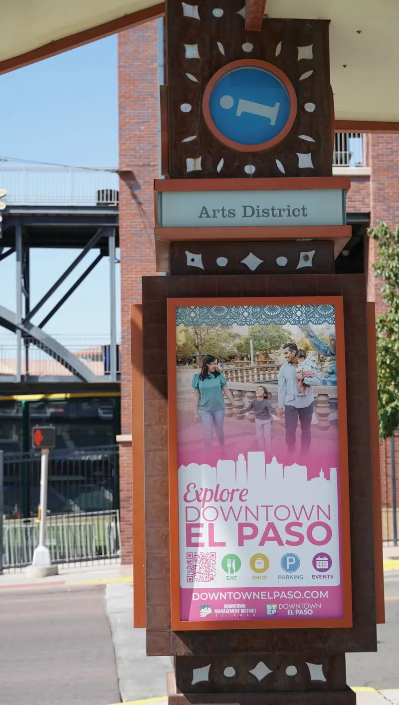 Arts District wayfinding sign with an Explore Downtown El Paso poster beside the downtown sidewalk